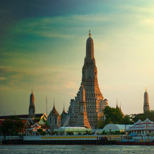 Stunning sunset view of Wat Arun temple by the Chao Phraya River in Bangkok, Thailand.