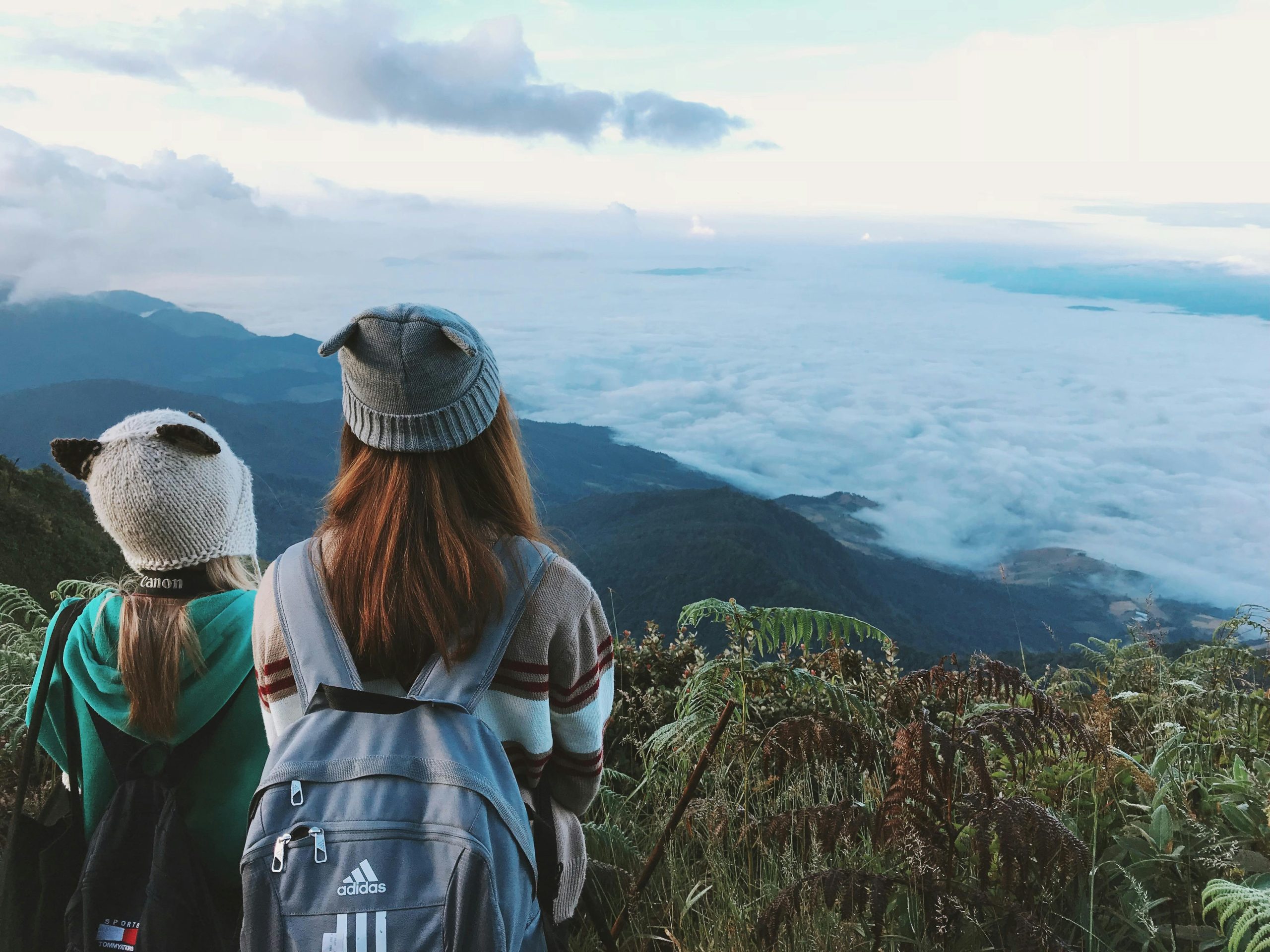 Two women with backpacks enjoy a scenic mountain view shrouded in clouds, ideal for travel enthusiasts.
